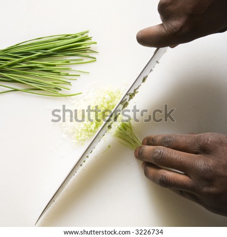 African-American male hands using large kitchen knife to chop fresh chives.