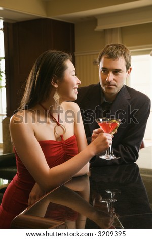 Taiwanese mid adult woman and Caucasian man at bar toasting martinis.