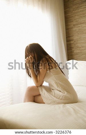 Pretty young Caucasian woman sitting on bed wearing nightgown.
