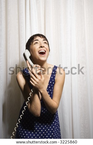 Pretty Caucasian young woman holding telephone receiver to ear and laughing.