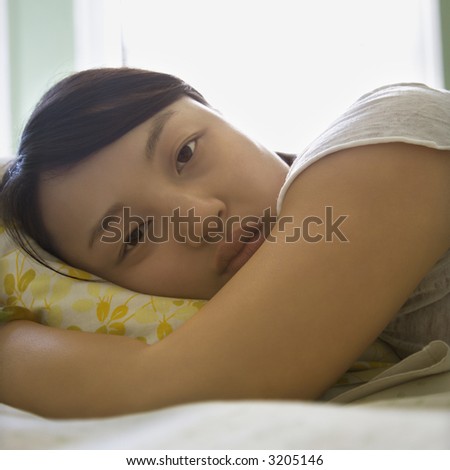 Portrait of pretty young Asian woman lying in bed with head on pillow making eye contact.