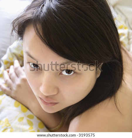 Head and shoulder portrait of pretty young Asian woman lying in bed making eye contact.