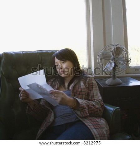 Pretty young Asian woman sitting in green chair reading letter.