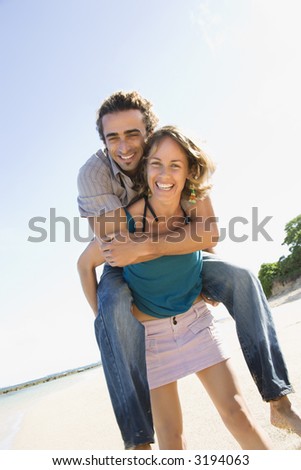 Mid-adult Caucasian woman giving man piggyback ride on beach.