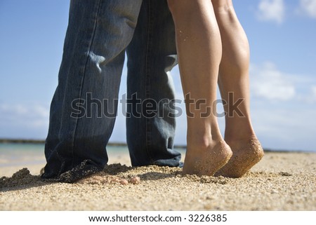 Feet and legs of mid-adult Caucasian couple standing together on beach.