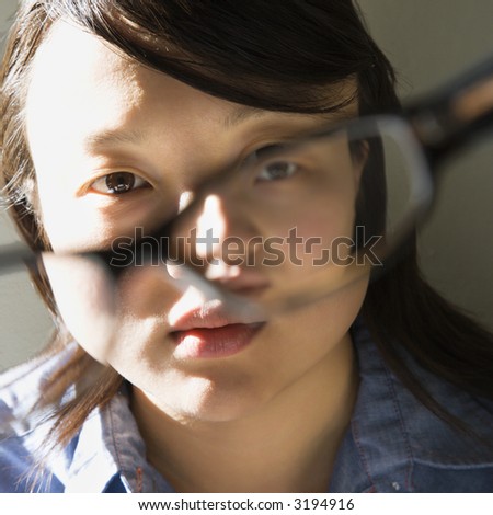 Head and shoulder portrait of pretty young Asian woman holding eyeglasses.