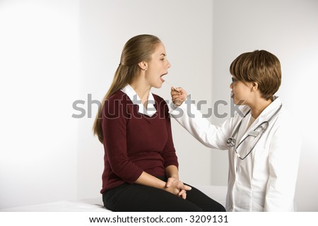 African American middle-aged female doctor examining Caucasian mid-adult female patient with tongue depressor.