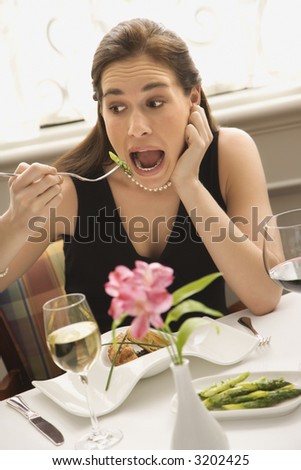 Mid adult Caucasian woman making exaggerated expression while eating with fork to mouth.