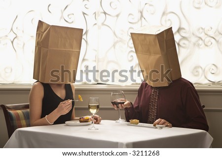 Mid adult Caucasian couple dining in a restaurant with paper bags over heads.