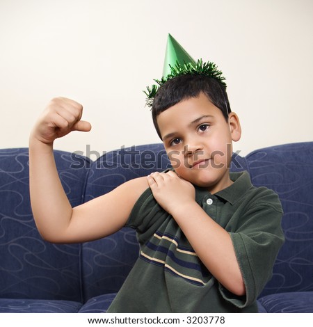 stock photo : Hispanic boy wearing party hat playfully flexing arm muscle 