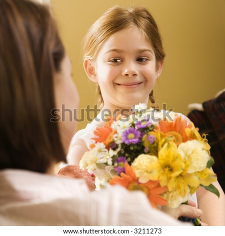 Caucasian girl giving mid adult mother flowers.