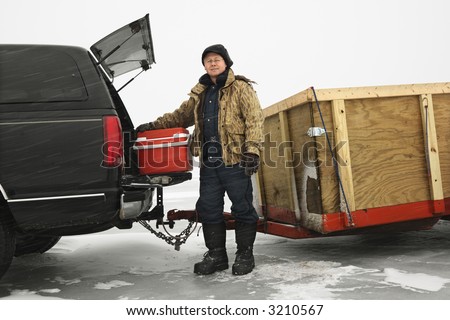 Caucasian man unloading cooler from truck with trailer on frozen lake going ice fishing in Green Lake, Minnesota, USA.