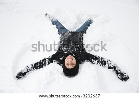 Caucasian mid adult woman making a snow angel in the snow.