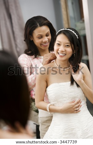 African-American friend helping place necklace on Asian bride.