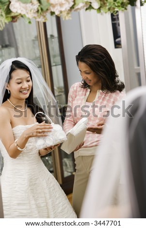 African-American woman helping Asian bride pick out handbag.