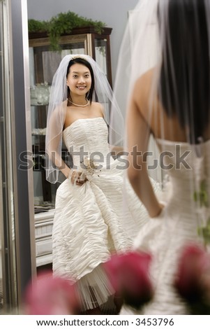 Asian bride admiring dress in mirror.