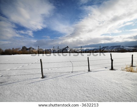 Barbed wire fence with snow covered ground and mountains in background.