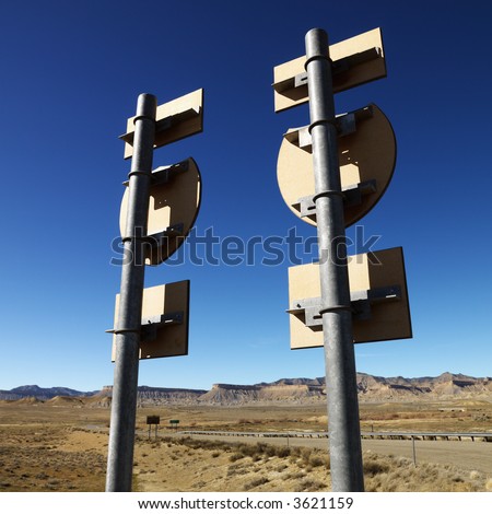 Two road signs on a post with guardrail and mountains in background.