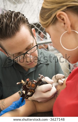 stock photo : Caucasian male tattoo artist tattooing Caucasian woman.