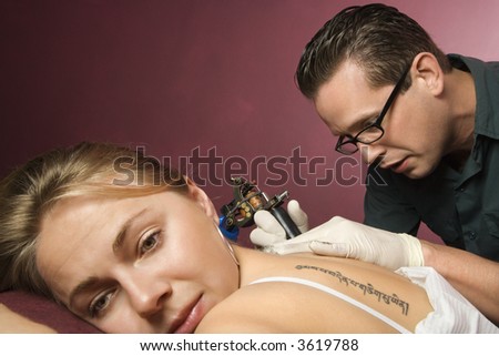 Caucasian male tattoo artist tattooing Caucasian woman.