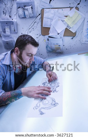 Caucasian male tattoo artist drawing tattoo on light table.