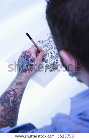 stock photo : Caucasian male tattoo artist drawing tattoo on light table.
