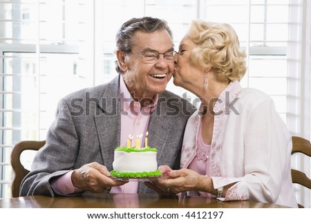 Mature Caucasian woman kissing mature Caucasian man while holding birthday cake.