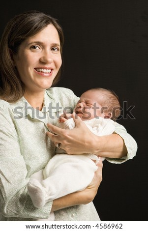 Mother smiling holding baby against black background.