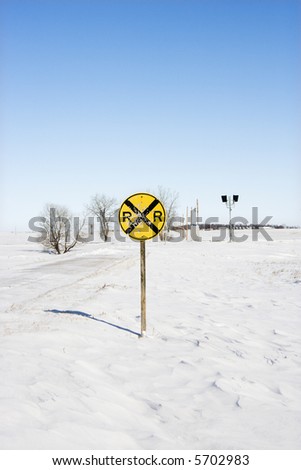 Railroad crossing sign in snow covered rural landscape.