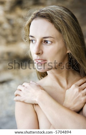 Mid adult Caucasian nude woman with arms crossed on shoulders looking to side.