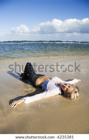 Pretty Caucasian woman lying on water\'s edge on beach in Maui, Hawaii smiling.