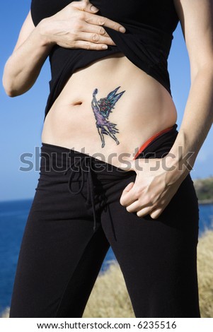 Caucasian woman exposing tattoo of fairy on stomach.