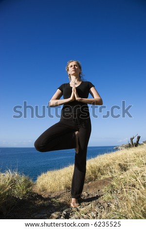 Caucasian mid-adult woman standing on Hawaiian coast in Yoga tree position.