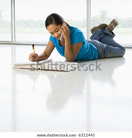 stock photo Asian preteen girl lying on floor doing homework while talking 