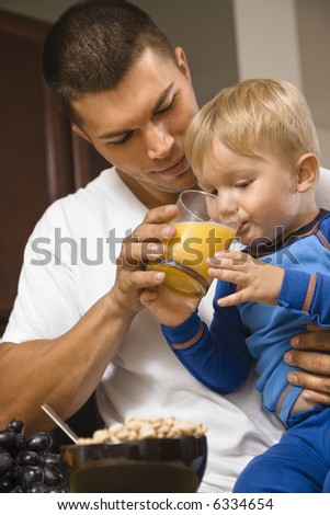 Caucasian man helping toddler son drink juice.