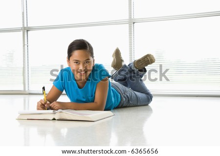 stock photo Asian preteen girl lying on floor doing homework looking up at 