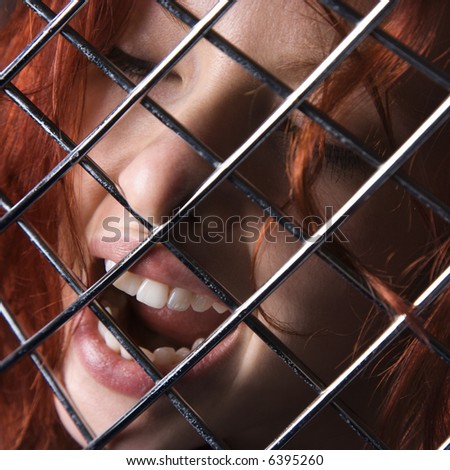 Pretty redhead young woman face with mouth open behind metal pattern.