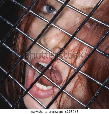Pretty redhead young woman face with mouth open behind metal pattern.