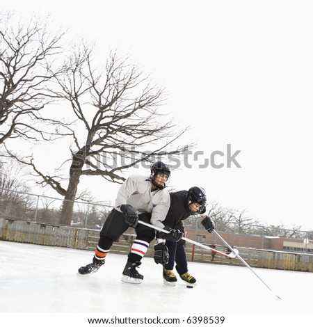 Two boys in ice hockey uniforms playing hockey on ice rink.