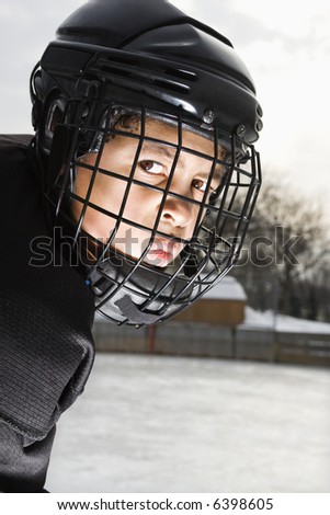Ice hockey player boy in uniform and cage helmet making mean face.