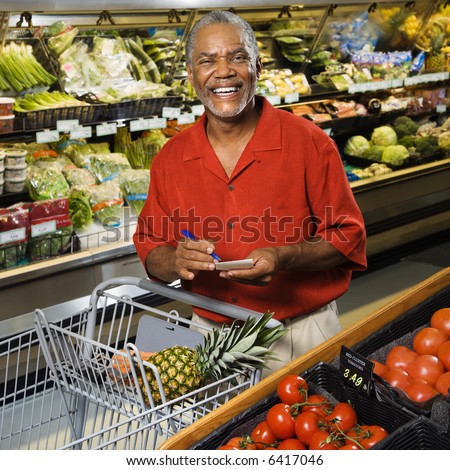 Middle aged African American man in grocery store holding shopping list and smiling at viewer.