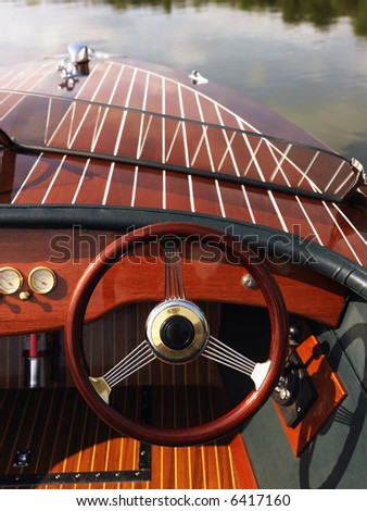 Wooden boat with steering wheel and dashboard floating in gentle water.