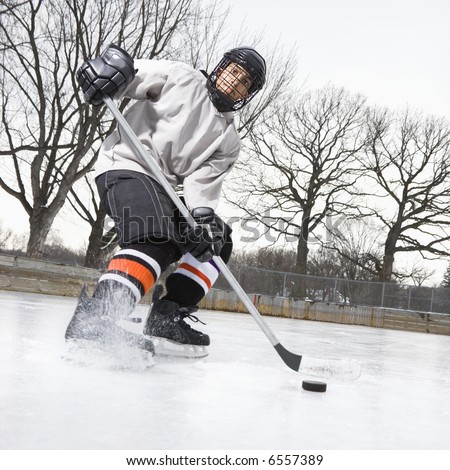 stock photo : Boy in ice hockey uniform skating on ice rink moving puck.