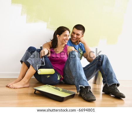 stock photo : Couple sitting on floor smiling in front of partially painted wall in home.