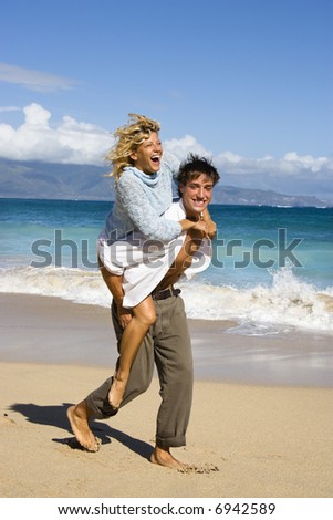 Woman riding piggyback on man while both smile and laugh on Maui, Hawaii beach.