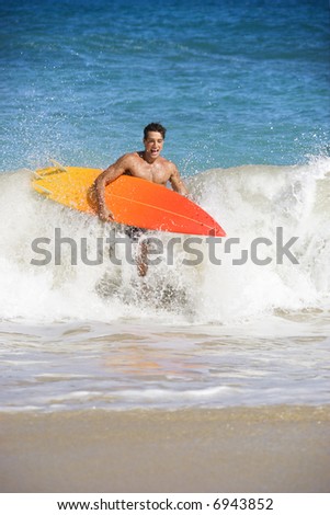 Attractive young man running out of water carrying surfboard in Maui, Hawaii.