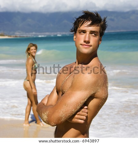 Handsome man standing on Maui, Hawaii beach with woman in background.