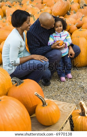 Parents and daughter picking out pumpkin and smiling at outdoor market.