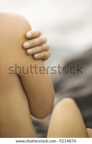 Close up of nude young Caucasian womans hand on shoulder.