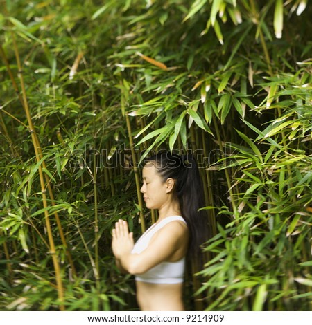 Half length portrait of Asian American woman in fitness attire standing in yoga position in bamboo forest in Maui, Hawaii.